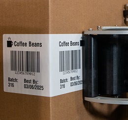 A brown box is being labelled with an automated label applicator